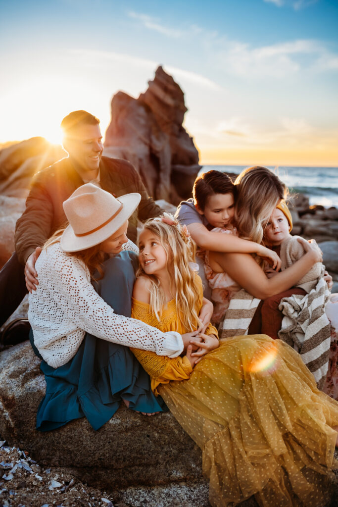 Family Photography, family of six snuggled together on beach with sun behind them